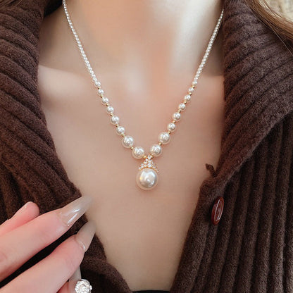 Luxury pearl jewelry set featuring a pearl necklace with a large central pendant worn with a brown textured sweater